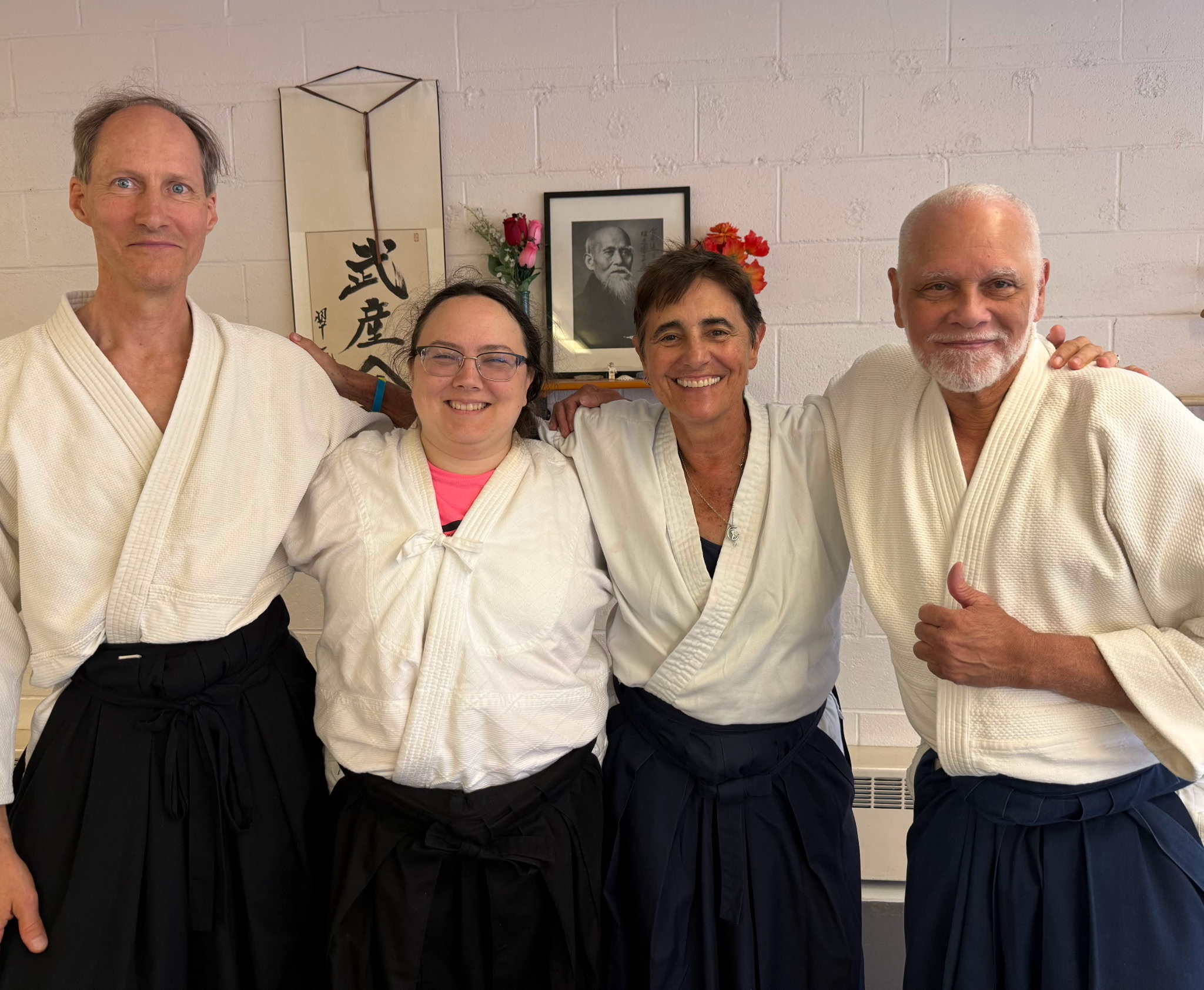Four aikidoka in hakama at the dojo, beneath a portrait of O-Sensei