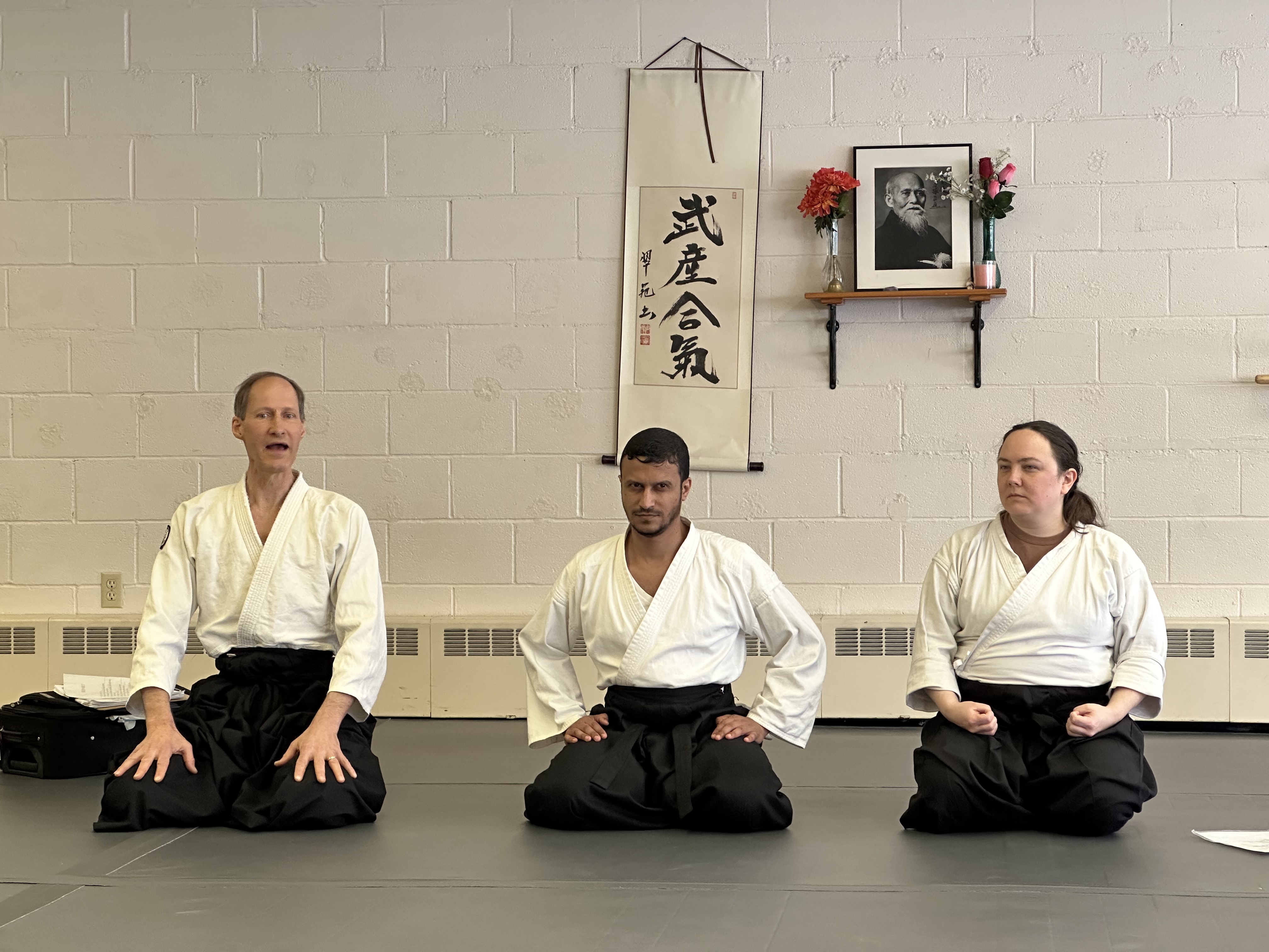 Students in seiza beneath calligraphy and a portrait of O-Sensei